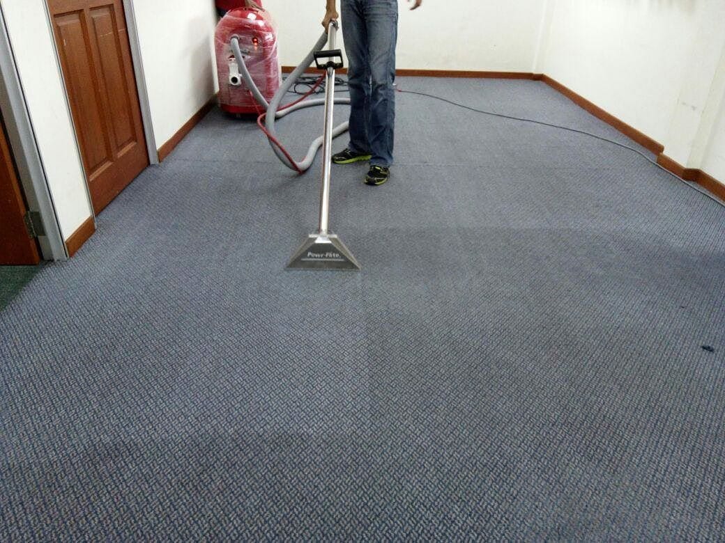 Open Room With A Person Cleaning A Dark Gray Carpet
