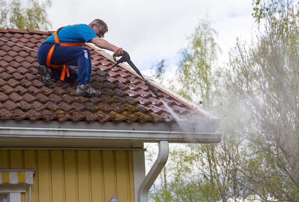 Caucasian man is washing the roof with a high pressure washer. H