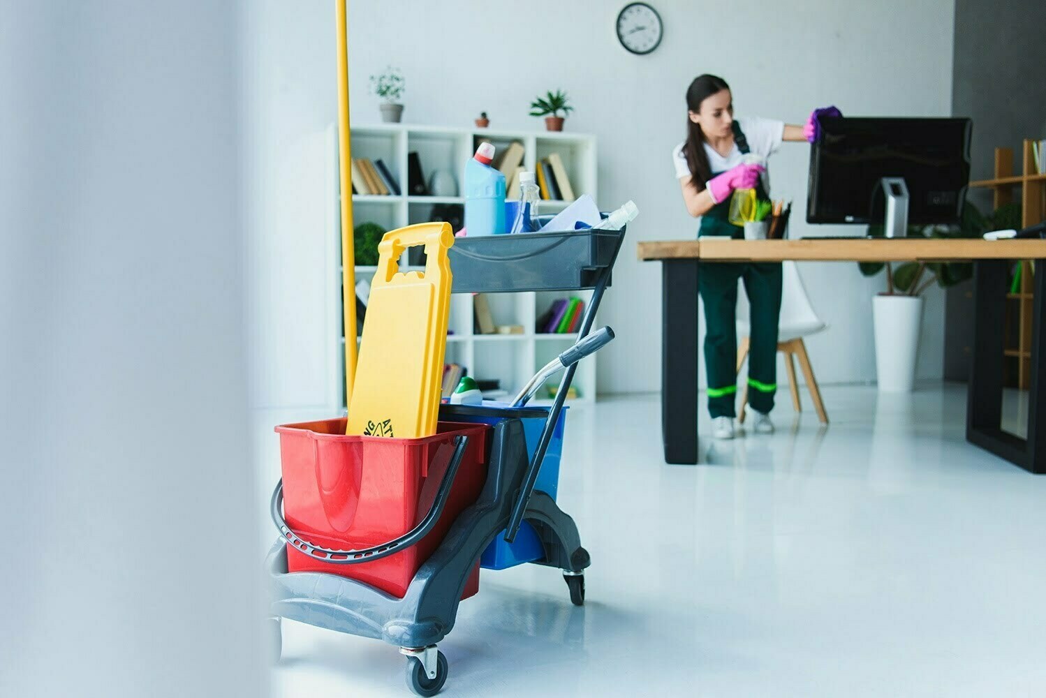 young female janitor cleaning office with various cleaning equip